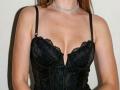 Jumiera wearing a black lace corset with a deep cleavage, showing her tits. She has a sparkly choker and straight brown hair, with black straps on her shoulders.