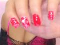 ExquisDunya's red glittery nails with shiny polish, holding a clear plastic tube, wearing black lace and pink lingerie, showing a bit of her tits and fishnet thigh.