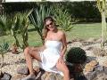 LaFrancaise with tan skin, brown hair in a ponytail, wearing a white strapless dress, sitting with legs spread, showing her pussy, in a garden with cacti and rocks.