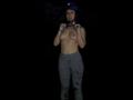 MollyMarmalade, topless, with small tits, wearing grey, dirty, flower-patterned pants, and a blue helmet, holding her shirt, standing in dark, against a black background.