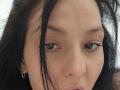 JoliDanielle's face with brown eyes, black eyelashes, and straight black hair covering part of her face. She has light skin, small gold hoop earrings, and a neutral expression.