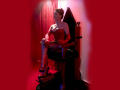 MaitresseElsa with big tits, in a red latex dress and gloves, sitting on a black wooden chair, legs crossed, red high heels, red curtain, red light, seductive look.