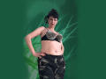 MaitresseElsa with short black hair, wearing a black bra with metal studs, and camo pants, standing with hands on hips, looking down, green background.