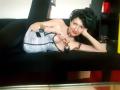 MaitresseElsa with black hair, red lipstick, and silver corset, holding a black ball, lying on a black couch, wearing black pants and a silver bracelet, looking at camera.