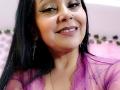 Zaria69 with long black hair, purple eyeliner, smiling, wearing a sheer purple top, nose ring, and dangling earrings, showing a cute face and a gold necklace.