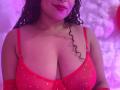 LolyMarce with curly black hair, red lipstick, and red sparkly bra showing her large tits. She's wearing red gloves, and the image has purple and pink lighting.