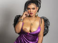 AliceJelanni with large breasts, wearing a shiny purple dress, black feathered wings, gold earrings, and bracelets, touches her face seductively, with a confident expression, highlighting her cleavage.