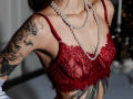 SophieKitty's red lace bralette, showing her tits, with a long pearl necklace, and a tattooed arm. Her tits are small to medium, and her tattoos are black ink.
