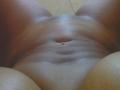 Ebonydaniels' belly button with a small piercing, showing a slight navel indentation, surrounded by her brown, shiny, smooth-assed, and brown-boobed thighs.