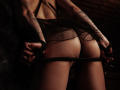 SophieKitty's butt is exposed, wearing black sheer lingerie, pulling down her panties with black rope, arms tattooed, dark, moody lighting, her hands gripping the rope.