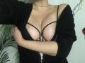 LadyMiller's large tits in a black bra, covered by a black zip-up jacket, with her right arm crossing over her chest. She's wearing a thin black choker.