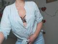 LadyMiller wearing a striped, button-down shirt tied at the waist, exposing black bra straps and her tits. She's holding her shirt, with blue pants and a slightly tilted head.