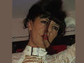 MaitresseElsa has dark hair, red lipstick, and a white leather collar with a buckle. She's wearing lace and looking seductively at the camera. Her tits are partially visible.