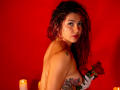 AntonelaRiveiro with curly red hair, holding a rose, has tattoos on her arm, and is topless, showing her tits. Red background with candles. Her ass is visible.