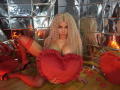 SandraXSeins with long blonde curly hair, big tits, red thigh-highs, and black heels, holding a red heart pillow, sitting on a wooden floor, surrounded by red heart decorations.